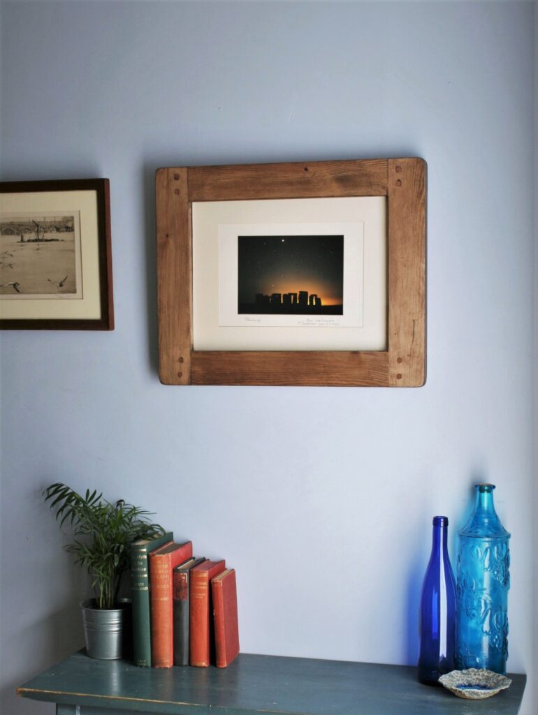 Large A3 picture frame in chunky natural wood, on the wall with blue glass ornaments and vintage books below