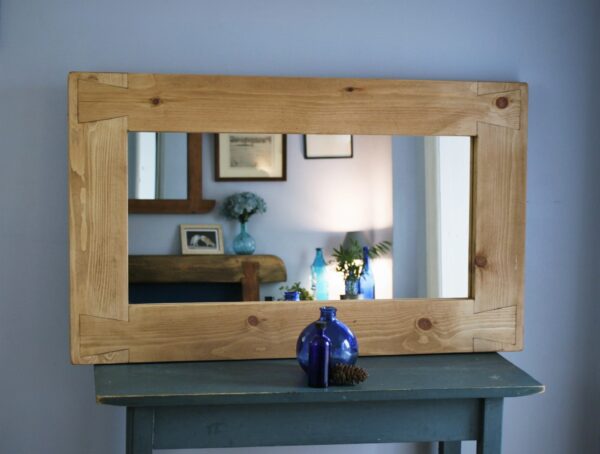Chunky wooden mirror, rustic cottage farmhouse style, on a table with a blue glass vase in front.