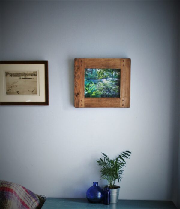 Chunky wooden picture frame for 8 x 10 inch photo or art print. Handmade in Somerset UK, view of dark wood tone option with plants and glass vases on a table beneath.